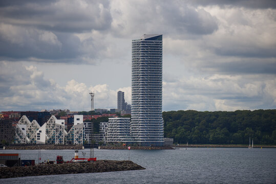 Aerial view of the Lighthouse building and the surrounding modern architecture in the Aarhus O district, set against a cloudy sky and the harbor waters in Aarhus, Denmark.