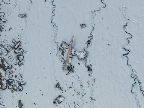 Aerial view of the historic C-124 plane wreckage on the icy surface of Bomber Glacier, surrounded by snow and winding glacial streams in Matanuska-Susitna Borough, Alaska, United States.