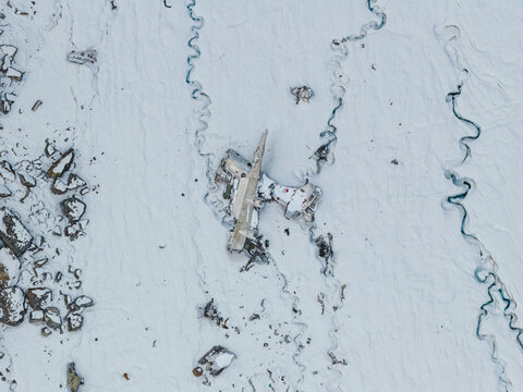 Aerial view of the wreckage of a plane on the snow-covered Bomber Glacier, surrounded by winding meltwater channels and rocky terrain in Matanuska-Susitna Borough, Alaska, United States.
