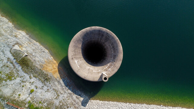 Aerial view of the Stubo Rovni Dam spillway, a large concrete funnel structure surrounded by deep green reservoir water and rocky shorelines in Stubo, Kolubarski okrug, Serbia.