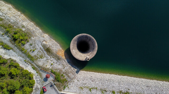 Aerial view of the Stubo Rovni Dam spillway, a large concrete funnel structure set within a reservoir surrounded by rocky banks and green vegetation Stubo, Kolubarski okrug, Serbia.