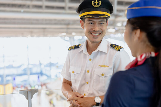 Asian Pilot Smiling Laughing Friendly Talking with Female Air Hostess in Airport Terminal Background