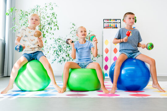 Kids practice balance, coordination and motor skills with maracas while sitting on exercise balls during an occupational therapy activity.