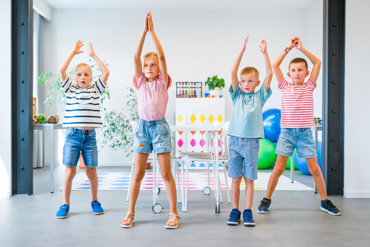 Group of kids performing coordinated movement exercises together, developing motor skills, concentration, balance and body coordination during a classroom activity.