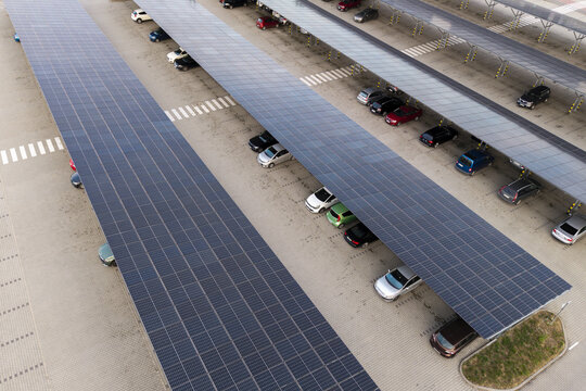 Aerial view of a parking lot featuring rows of cars sheltered by large photovoltaic solar panel carports in Poland.