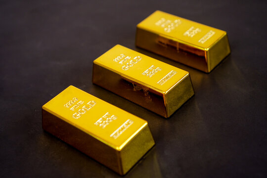 Three polished gold bars gleam softly against a dark background. Each bar bears engraved markings, indicating purity and weight. They rest in a diagonal line, creating a sense of balance and value