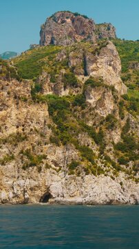 Tall pale crag riddled with caves standing over calm water in Amalfi coast