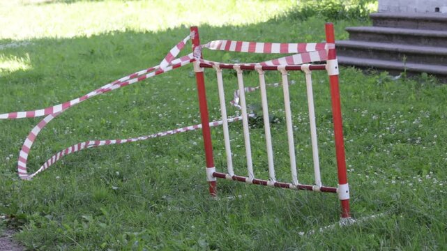 A portable plastic barrier with red vertical posts and white slats stands on a lush green lawn scattered with tiny white flowers