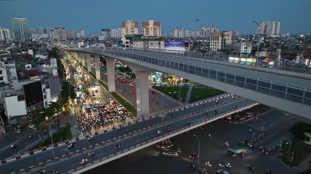 Aerial cityscape of Hanoi showing the elevated Ring Road 3 highway crossing Giai Phong Street, with busy traffic, illuminated buildings, and urban streets at dusk.