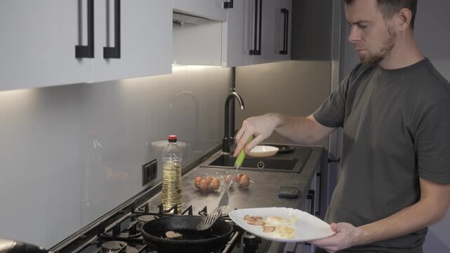 Man handling eggs beside gas cooktop in modern kitchen with cast iron skillet, open carton, oil bottle, white bowl, reflective backsplash, and focused preparation for cooking