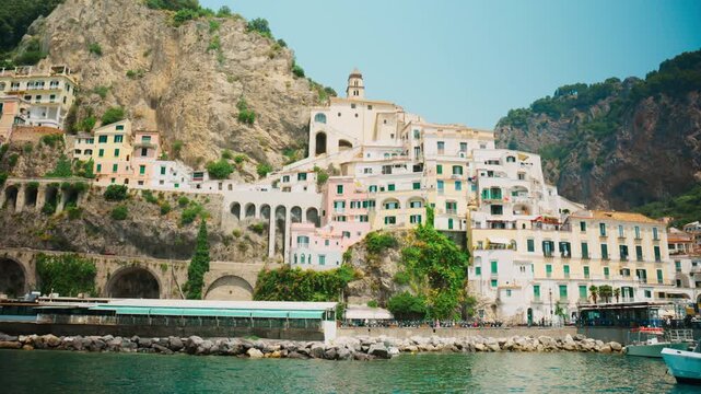 Boats tied along a stone jetty beneath a tightly packed old town Amalfi