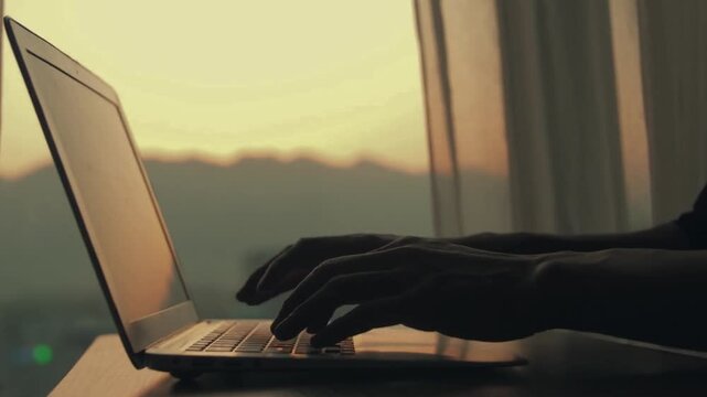 Hands typing on a laptop keyboard in warm golden window light, remote work and freelance business concept, 4K