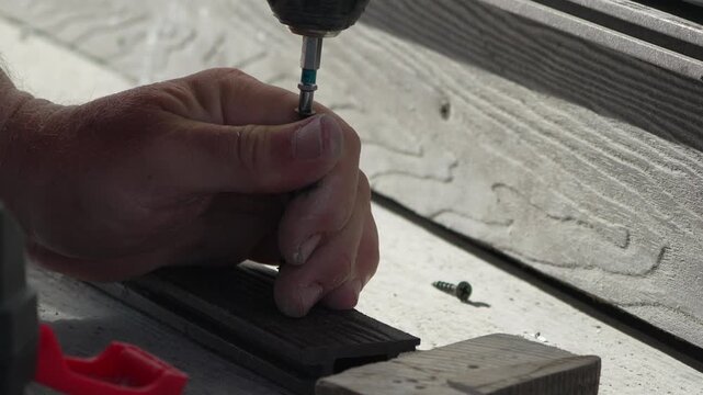Screwing deck fasteners using a cordless power drill on composite board outdoors. Extreme close-up shot.