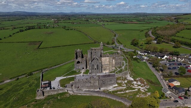 Aerial view of the historic Rock of Cashel, a medieval fortress and ecclesiastical site, surrounded by lush green fields and rolling countryside in Cashel, County Tipperary, Ireland.