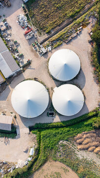 Aerial view of large circular biomethane reactors within a modern agricultural complex in San Giuliano Milanese, Lombardy, Italy.