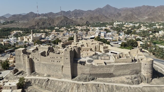 Aerial view of Bahla Fort, a historic UNESCO World Heritage site, surrounded by palm groves and the town of Bahlat in the arid landscape, Bahlat, Ad Dakhiliyah, Oman.
