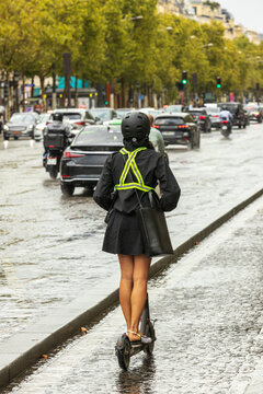Woman riding electric scooter with reflective vest on wet Paris street urban traffic sustainable mobility eco friendly commuting lifestyle