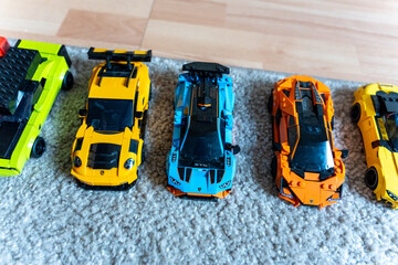Obraz premium Warsaw, Poland - Sep 4, 2026: Row of four LEGO Technic model cars in green, yellow, blue and orange on a gray rug