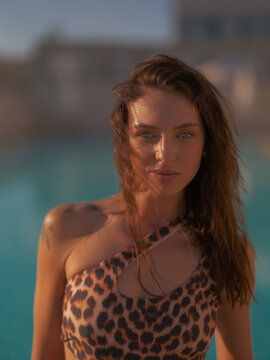 Portrait of young woman in leopard swimsuit standing poolside looking at camera