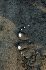 A person stands barefoot on wet dark volcanic sand along a tropical beach in Costa Rica. © jiriviehmann