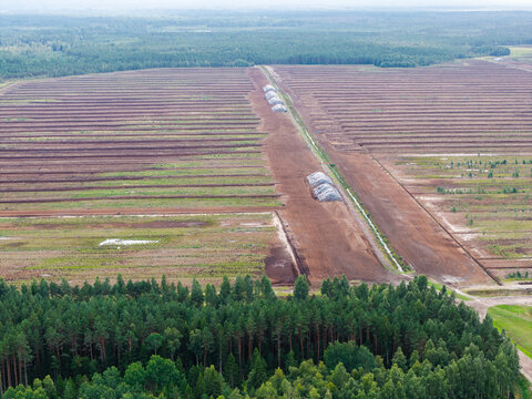 Aerial view of Lielsalu purvs showing extensive peat extraction fields with rows of harvested peat and plastic-covered piles surrounded by forest in Lielsalas, Talsi Municipality, Latvia.