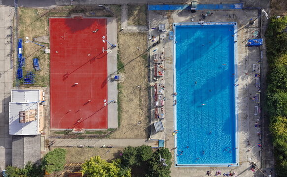 Pancevo, Vojvodina, Serbia - 28 August 2026: Aerial view of the sports center featuring a red basketball court and a large blue swimming pool with people swimming.