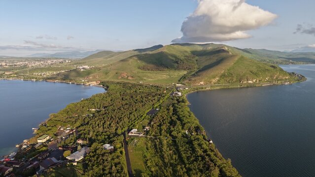 Aerial view of Lake Sevan with its lush green peninsula extending into the water, surrounded by rolling hills under a clear blue sky in Sevan, Gegharkunik Province, Armenia.