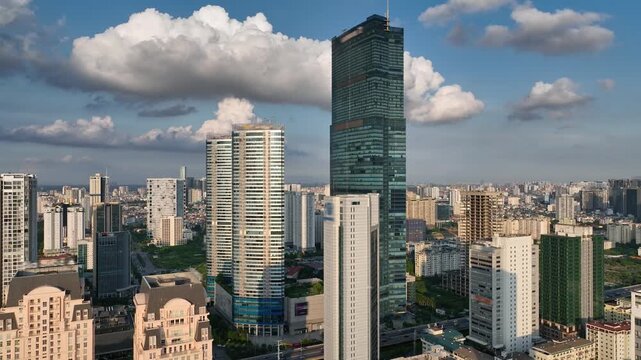 Aerial view of Hanoi, Vietnam, showing the Me Tri&ndash;Pham Hung intersection, dense residential buildings, modern skyscrapers, and dramatic clouds over the city.