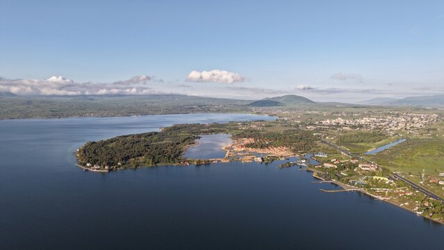 Aerial view of Lake Sevan with its expansive blue waters, lush green shoreline, and the town of Sevan in the distance under a clear sky in Sevan, Gegharkunik Province, Armenia.