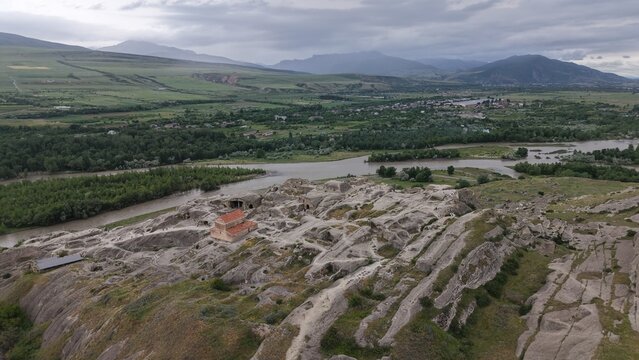 Aerial view of Uplistsikhe ancient rock-hewn town with its historic church, rugged sandstone formations, and the Mtkvari River in the green valley Kvakhvreli, Shida Kartli, Georgia.