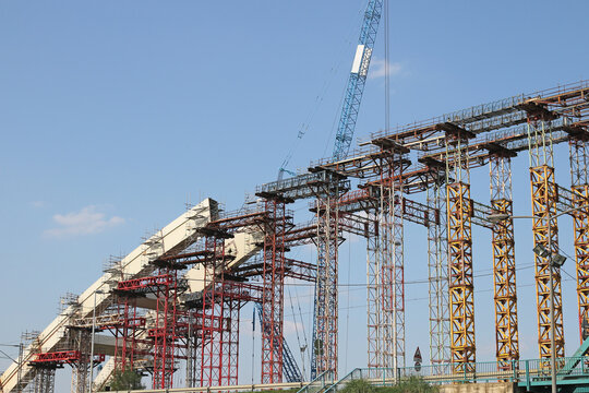 Massive Bridge Construction Site with Scaffolding and Crane Under Blue Sky