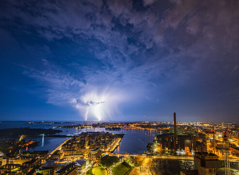 Aerial view of a lightning storm illuminating the night sky over the Helsinki coastline and urban landscape, featuring the Kalasatama district, city lights, and the sea in Helsinki, Uusimaa, Finland.