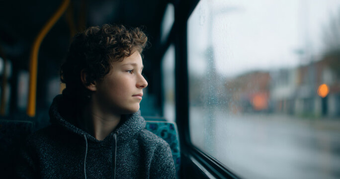 Teen boy looking out rainy bus window