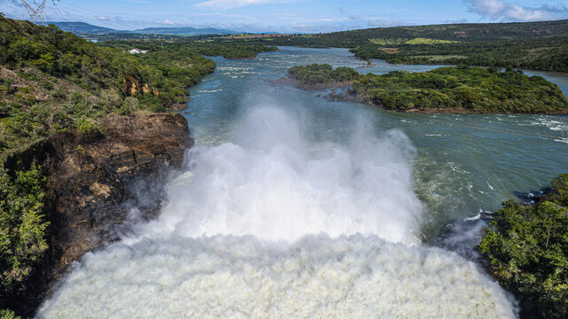 Aerial view of Furnas Hydroelectric Plant with powerful water discharge creating mist over the river surrounded by lush green hills and vegetation in Rio Grande, Minas Gerais, Brazil.