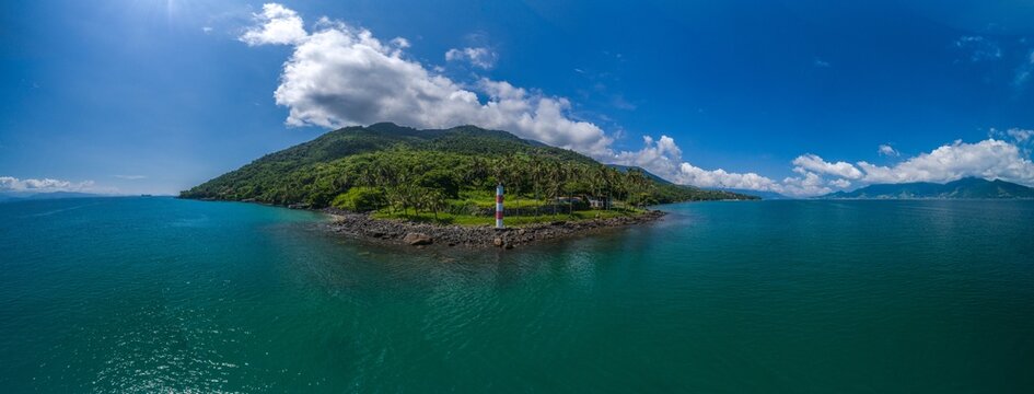 Aerial view of Farol Ponta das Canas lighthouse on a lush green coastal headland surrounded by turquoise ocean waters in Ilhabela, Sao Paulo, Brazil.