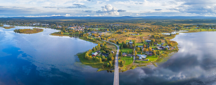 Aerial view of the village of Vittangi along the Torne River, with traditional red houses, green fields, and a bridge crossing the water in Vittangi, Norrbotten County, Sweden.