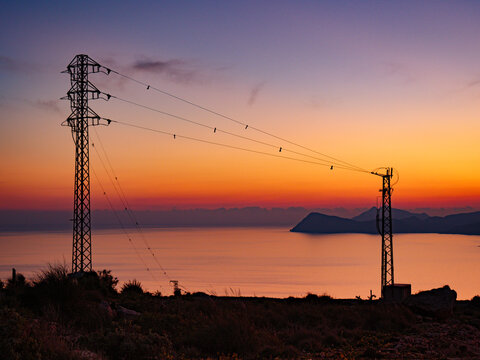 High voltage towers on coast at sunset