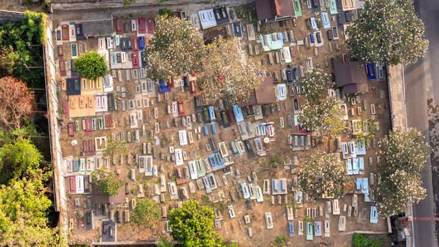 Aerial view of a cemetery with numerous colorful tombstones and graves scattered across the dirt ground, surrounded by trees in Surakarta, Central Java, Indonesia.