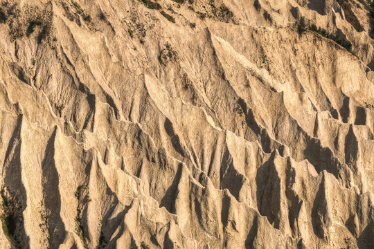 Aerial view of the dramatic, eroded clay formations known as the Calanchi, featuring sharp ridges and deep gullies under bright sunlight in Ripatransone, Marche, Italy.