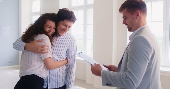 Happy young embracing after successful real estate deal and signing contract. Smiling man and woman shaking hands with real estate agent and celebrating agreement and property purchase or rent