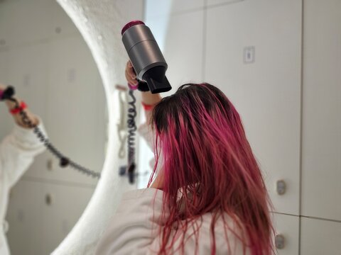 Woman drying her long pink hair with a blow dryer in a modern bathroom