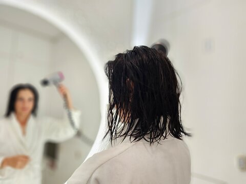 Person drying hair in bathroom with hairdryer in hand