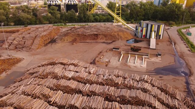 Aerial view of a timber yard with stacked logs, a woodchip pile and a loader feeding chips into a pit at a paper mill
