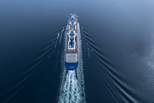 Bute, Scotland - 27 July 2022: Aerial view of a large cruise ship sailing through calm blue waters, leaving a white wake behind it.