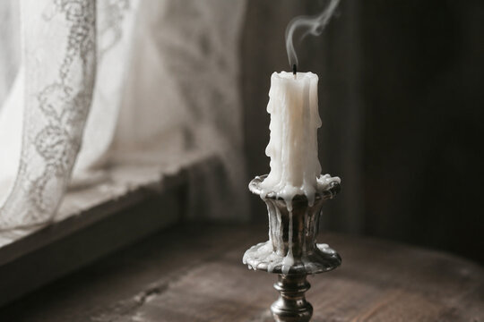 A single extinguished white candle with wax drippings on a tarnished holder.