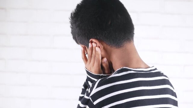 Young asian man experiencing ear pain from behind, suffering from otitis media or other ear problem on white background