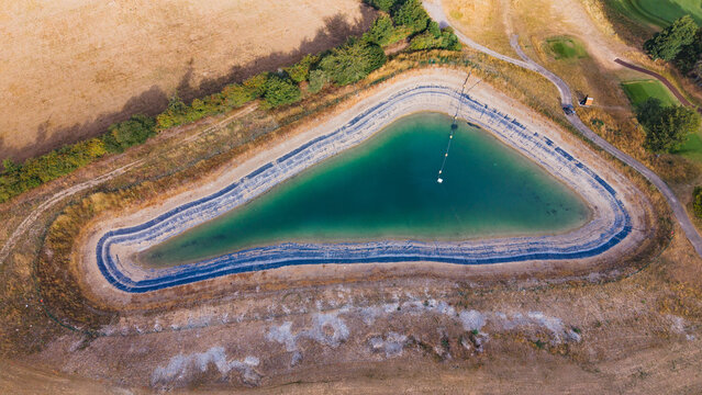 Basingstoke, United Kingdom - 17 August 2026: Aerial view of Basingstoke Golf Club featuring a turquoise water hazard surrounded by dry grass and golf course pathways.