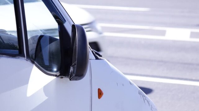 Sharp close-up of white car's side mirror and fender with orange reflector; blurred purple car in background creates depth