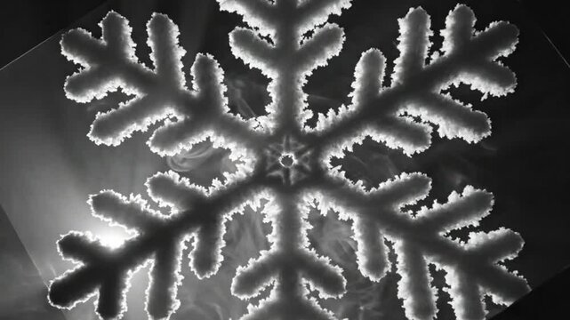 Black and white close up of a beautiful snowflake structure with illuminated edges and surrounding wispy smoke