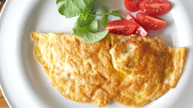 Close-up video of golden brown omelet served with fresh cherry tomatoes and arugula on white plate